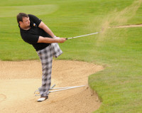 photograph of a golfer swinging a shot out of the sand of a bunker elegantly using his one leg to balance