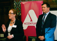 Jo Nolan and Damian Collins standing facing forwards giving a speech with the Accentuate banner behind them, in the highly decorative room with wooden panels in the Houses of Parliament