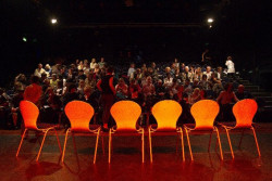 photo of empty chairs on a stage with an audience